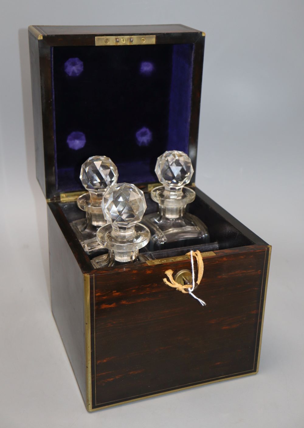 An early Victorian coromandel and brass bound four division decanter box, the lid inset with monogram, enclosing three decanters, heigh